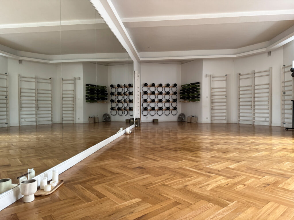 Sala do ćwiczeń w siedzibie Dobrzemitu: duża przestrzeń z parkietem, lustrem ściennym i sprzętem do treningu na ścianach